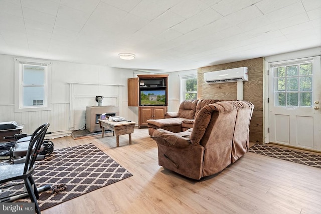 living area with a wall mounted air conditioner, light wood finished floors, and a healthy amount of sunlight