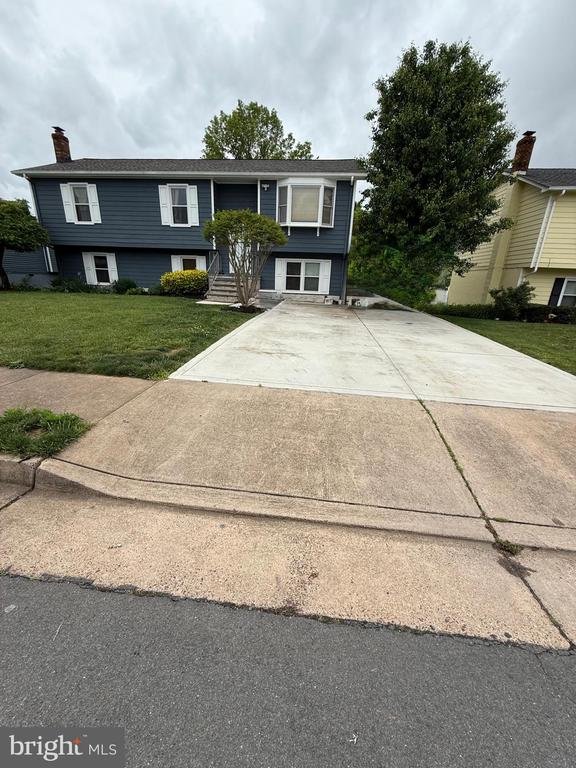  - split foyer home with a front yard, concrete driveway, and a chimney