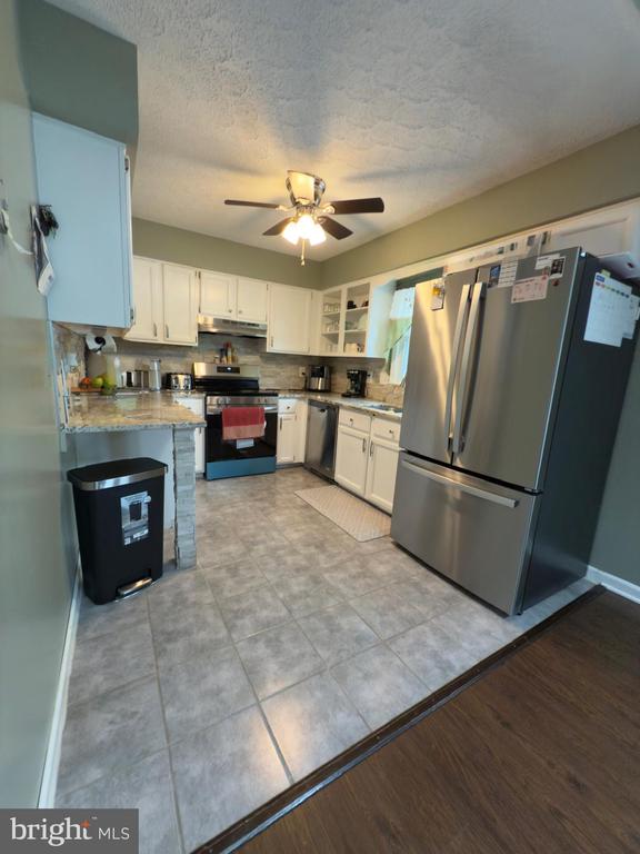  - kitchen featuring stainless steel appliances, under cabinet range hood, ceiling fan, white cabinetry, and a textured ceiling