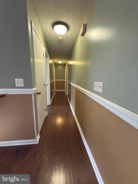  - hallway with wood finished floors, a textured ceiling, and baseboards