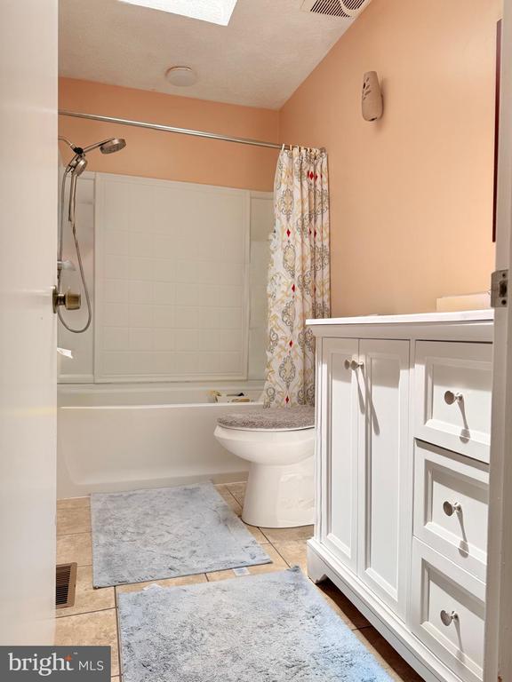  - bathroom with toilet, tile patterned floors, shower / bathtub combination with curtain, and vanity