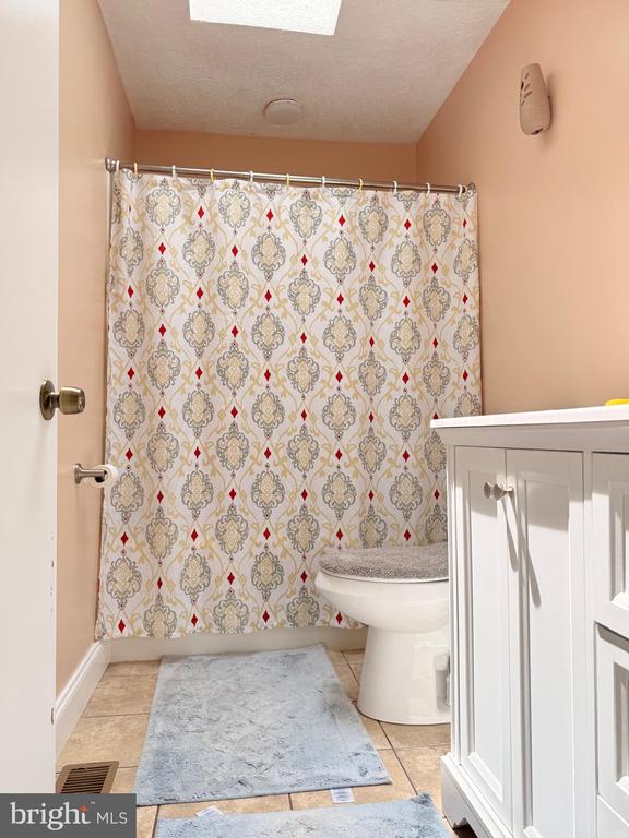  - bathroom featuring toilet, tile patterned floors, a skylight, baseboards, and a shower with curtain