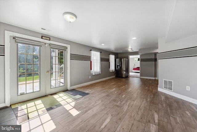 unfurnished living room with french doors, plenty of natural light, baseboards, wood finished floors, and recessed lighting