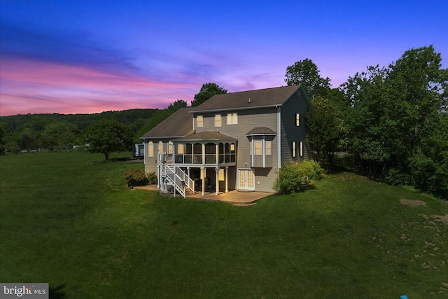 back of house at dusk with a patio area, a lawn, french doors, and a deck