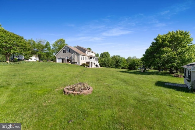 view of green lawn featuring stairway, a fire pit, and a deck