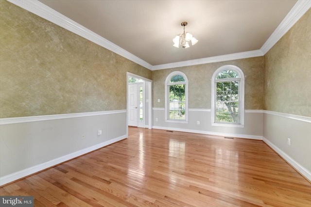 empty room with wood finished floors, a chandelier, baseboards, and crown molding