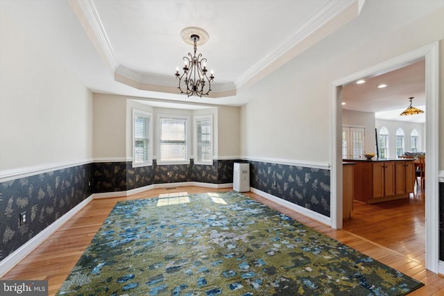 dining space featuring wallpapered walls, light wood-style flooring, a chandelier, crown molding, and wainscoting