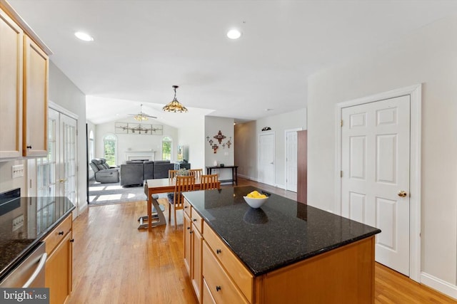kitchen featuring light wood finished floors, stainless steel dishwasher, a center island, open floor plan, and dark stone countertops