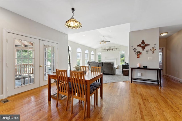 dining room featuring vaulted ceiling, light wood-style flooring, french doors, a fireplace, and ceiling fan