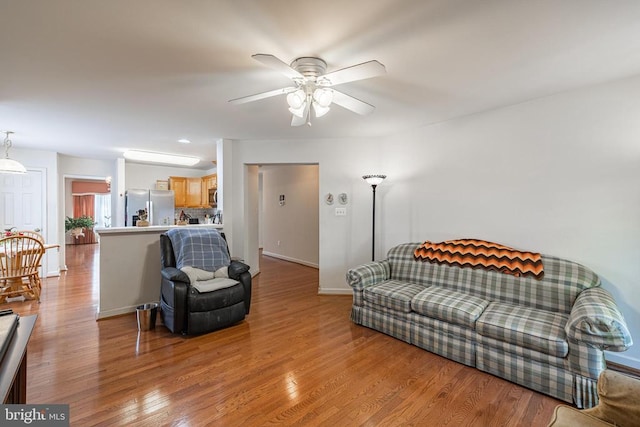 living area with ceiling fan, light wood finished floors, and baseboards