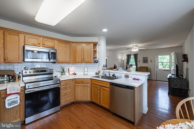 kitchen featuring appliances with stainless steel finishes, a peninsula, a sink, dark wood-type flooring, and recessed lighting