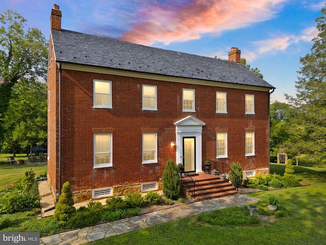 - colonial-style house featuring a chimney, a front lawn, brick siding, and a high end roof