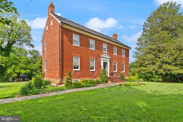  - colonial-style house featuring a chimney, brick siding, and a front lawn
