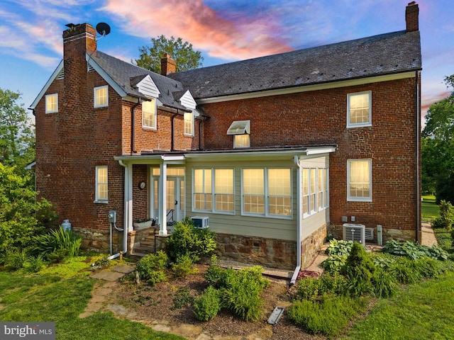  - back of house at dusk with a chimney, brick siding, a high end roof, and french doors