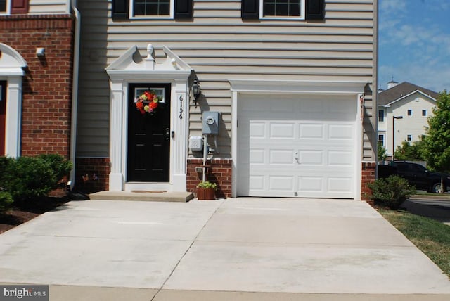  - property entrance with brick siding, driveway, and a garage