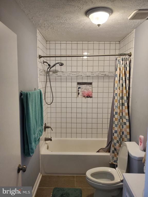  - full bath with tile patterned flooring, shower / bathtub combination with curtain, a textured ceiling, and vanity