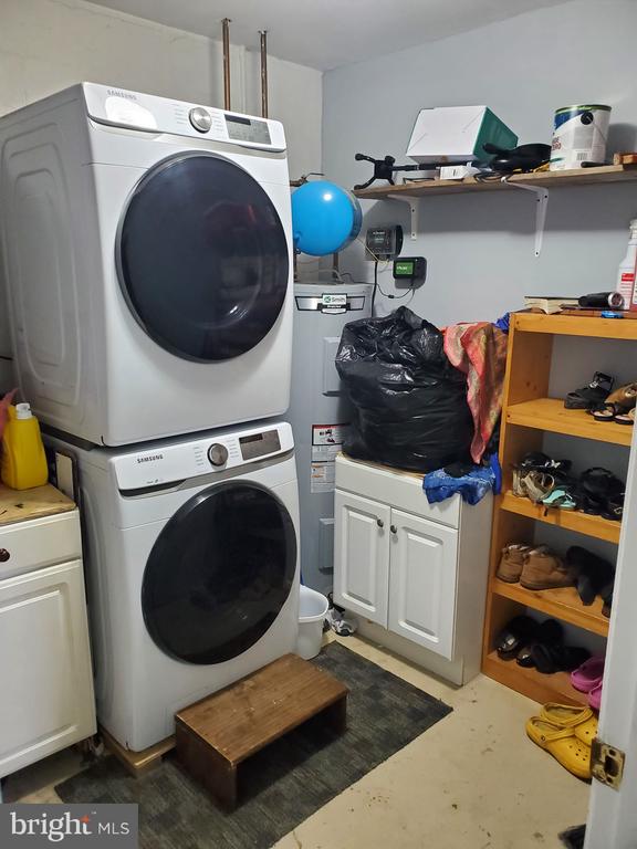  - laundry area featuring stacked washer / dryer, cabinet space, and electric water heater