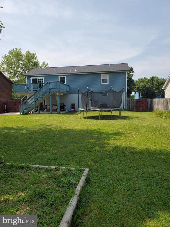  - back of property featuring stairs, a wooden deck, and a trampoline