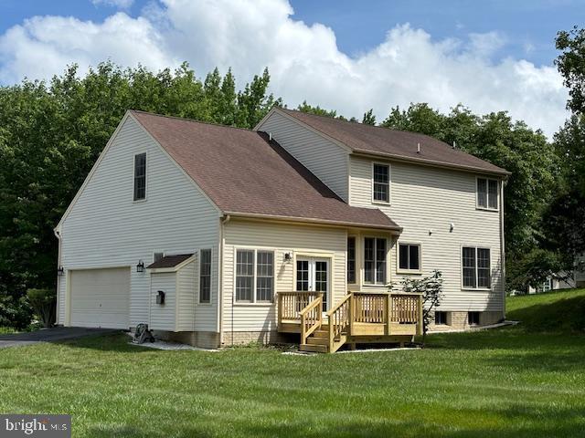 back of property featuring an attached garage, a wooden deck, a yard, and driveway
