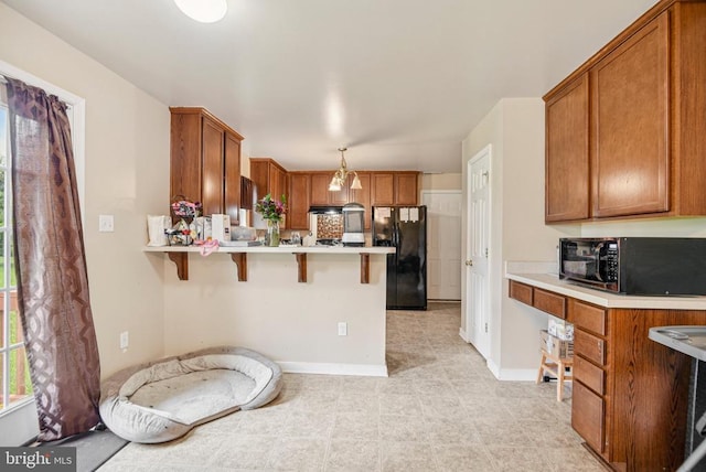  - kitchen with black appliances, a peninsula, a kitchen bar, light countertops, and brown cabinetry