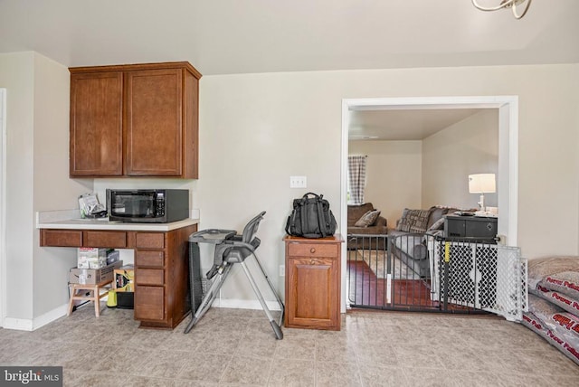  - kitchen with black microwave, brown cabinetry, open floor plan, and light countertops