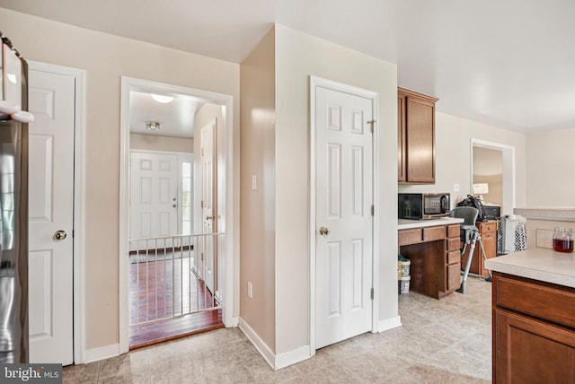  - kitchen featuring stainless steel microwave, light countertops, light tile patterned floors, and brown cabinetry