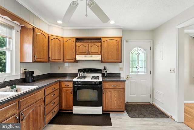  - kitchen with range with gas stovetop, under cabinet range hood, brown cabinetry, recessed lighting, and a textured ceiling