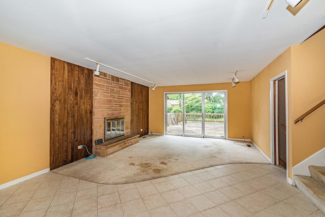 unfurnished living room with rail lighting, a stone fireplace, wood walls, and light carpet