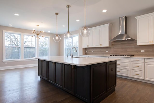 kitchen featuring a chandelier, wall chimney range hood, tasteful backsplash, a kitchen island with sink, and dark hardwood / wood-style flooring