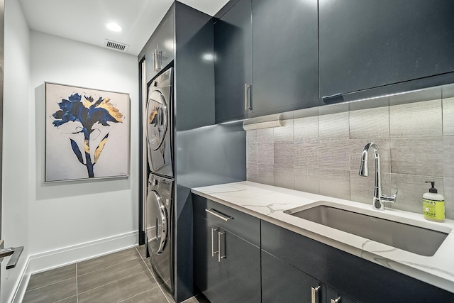 washroom with dark tile flooring, sink, and stacked washer / dryer