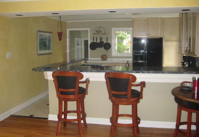 kitchen with light brown cabinetry, a breakfast bar, dark stone countertops, dark tile floors, and black fridge