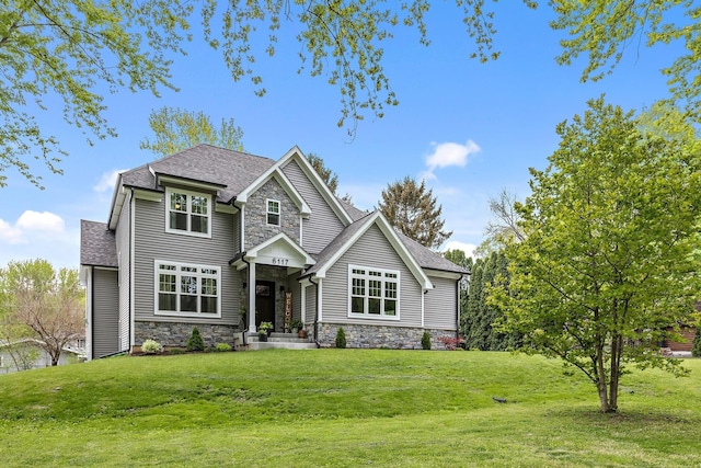 craftsman-style home featuring stone siding, a shingled roof, and a front yard