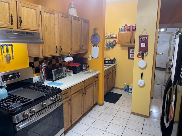 kitchen with light tile flooring, stainless steel gas range oven, tasteful backsplash, and fridge