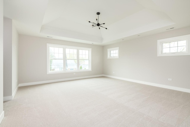 spare room with an inviting chandelier, light colored carpet, and a tray ceiling