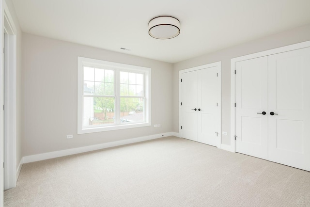 unfurnished bedroom with two closets and light colored carpet