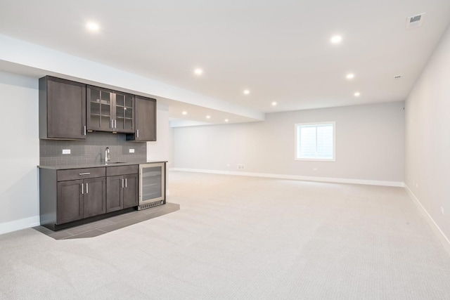 kitchen featuring light colored carpet, sink, dark brown cabinets, beverage cooler, and tasteful backsplash