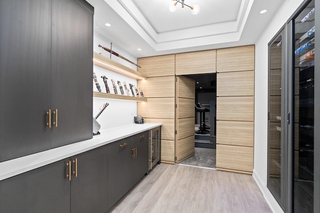 kitchen with a raised ceiling, light brown cabinetry, an inviting chandelier, and light hardwood / wood-style flooring