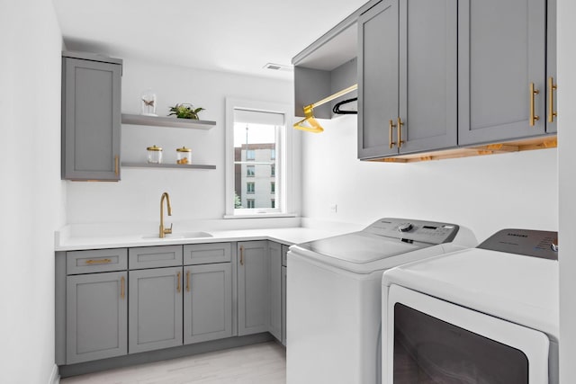 clothes washing area featuring light hardwood / wood-style floors, cabinets, sink, and washing machine and dryer