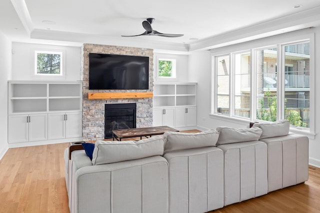 living room with a raised ceiling, a stone fireplace, ceiling fan, and light hardwood / wood-style flooring