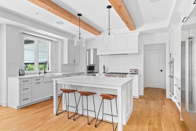 kitchen with decorative light fixtures, backsplash, beamed ceiling, light wood-type flooring, and white cabinets