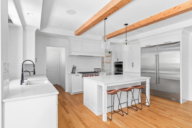 kitchen with hanging light fixtures, stainless steel appliances, light wood-type flooring, and sink