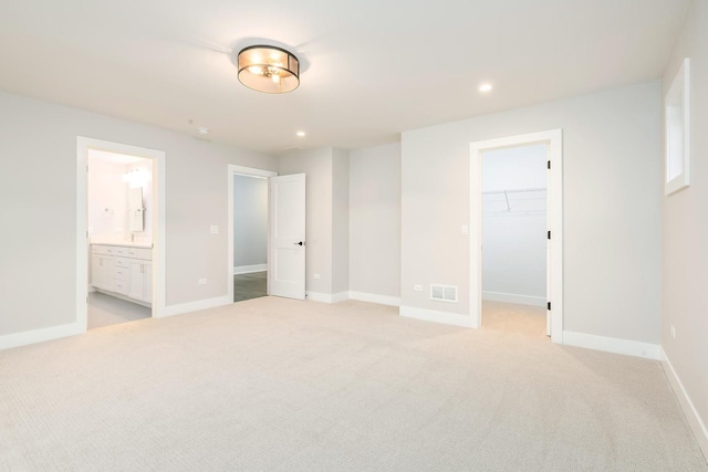 unfurnished bedroom with a closet, a spacious closet, ensuite bathroom, and light colored carpet