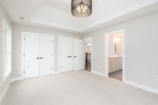 unfurnished bedroom with a raised ceiling, light colored carpet, and connected bathroom