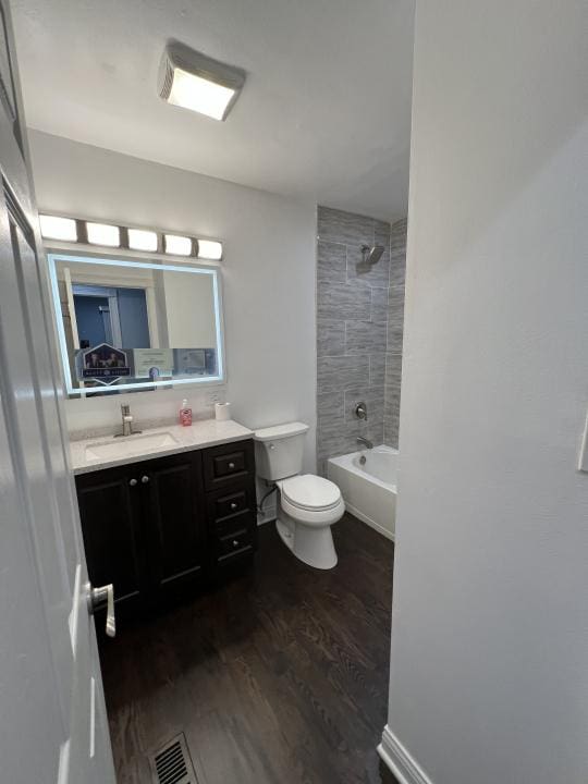 full bathroom with hardwood / wood-style flooring, tiled shower / bath combo, toilet, and vanity