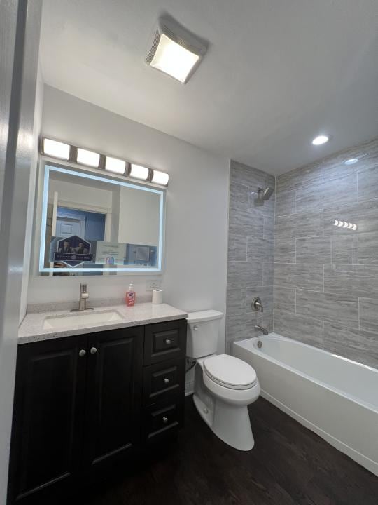 full bathroom featuring tiled shower / bath combo, toilet, wood-type flooring, and vanity