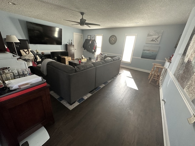 living room with a textured ceiling, ceiling fan, and dark wood-type flooring