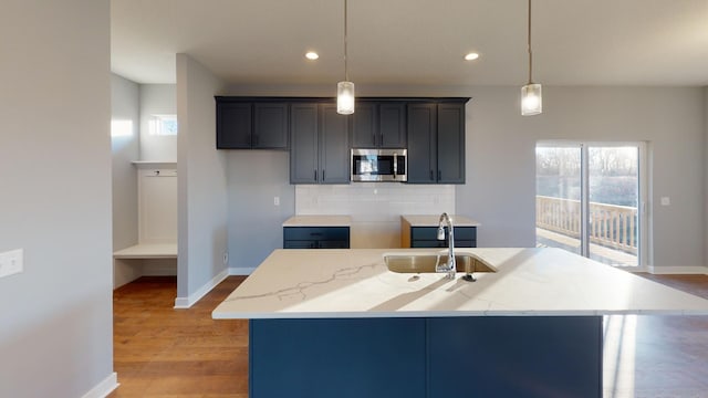 kitchen featuring sink, pendant lighting, light hardwood / wood-style flooring, a center island with sink, and tasteful backsplash