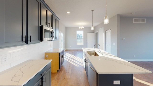 kitchen featuring appliances with stainless steel finishes, a kitchen island with sink, light wood-type flooring, and light stone countertops