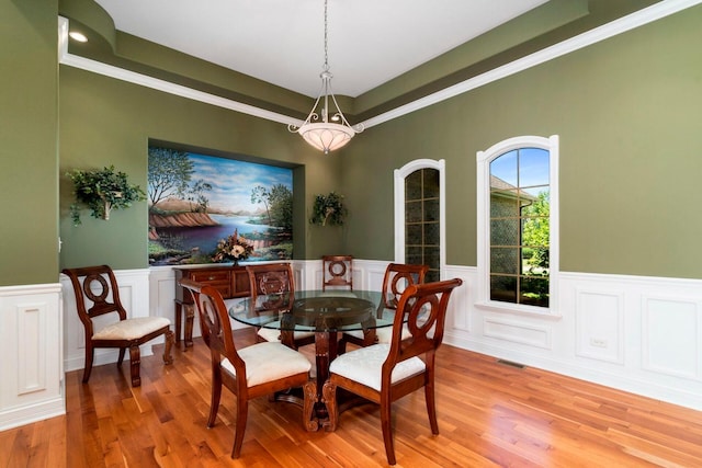 dining space with crown molding, light wood-type flooring, and a tray ceiling