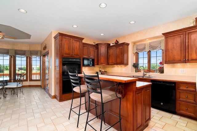 kitchen featuring black appliances, ceiling fan, a breakfast bar, sink, and a center island